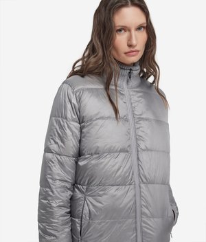 Kvinde med langt brunt hår iført en lysegrå quiltet dunjakke med lynlås foran og lommer, stående mod en hvid baggrund.