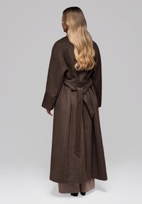 Abrigo largo a rayas marrón con mangas amplias, cintura ceñida con cinturón y textura suave. El diseño presenta una silueta suave y fluida.