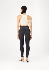 Melnas augstās skinny džinses ar gludu tekstūru, divām aizmugures kabatām un saplaisājušiem galiem, savienotas ar bēša krāsas īsu topu un atvērtām kurpēm ar papēdi.