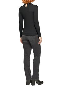 Schwarzes Langarmoberteil mit einem Rückenausschnitt im Schlüsselloch-Stil, kombiniert mit dunkelgrauen Slim-Fit-Jeans und schwarzen Plateaustiefeln.