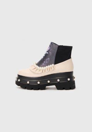 Chunky black platform boot with beige upper, pearl decorations along sole and cuff, ruffled trim, and printed dark panel on front.
