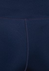 Granatowe legginsy z rozciągliwego materiału o gładkiej teksturze, z wysokim stanem i płaskimi szwami dla komfortu. Brak widocznych wzorów lub dodatków.
