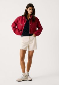Crvena traper jakna, crna majica, krem kratke hlače s rastrganim rubom i bež tenisice s svijetlim detaljima. Jednostavan, ležeran outfit.