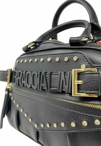 Borsa a mano in pelle nera con borchie dorate, un audace logo "BRACCIALINI" e una cerniera dorata. Superficie testurizzata e design strutturato.