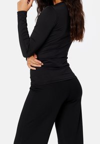Czarna bluzka z długim rękawem, uszyta z elastycznego materiału, o dopasowanym kroju i gładkiej fakturze, zestawiona z pasującymi czarnymi spodniami o luźnym fasonie.