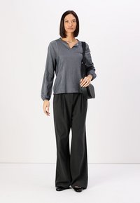 Striped blouse in black and white with long sleeves, paired with loose black trousers. Matte texture with minimalist design and flat shoes.