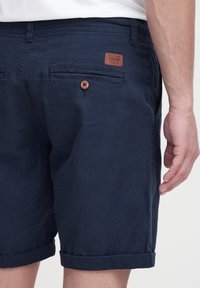 Shorts azul marino hechos de un tejido texturizado, con dobladillos enrollados, dos bolsillos traseros y una etiqueta de cuero marrón con detalles en relieve.