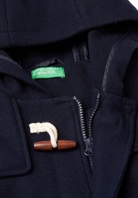 Abrigo de lana azul marino con capucha, presenta una etiqueta de marca verde, cierre de cremallera y un broche de madera con un cordón de color crema.