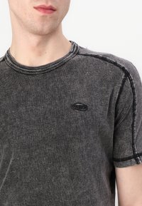Šedé tričko s krátkym rukávom vyrobené z mäkkej látky, s okrúhlym výstrihom, kontrastným šitím a malým logom na hrudi.