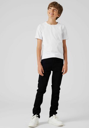 T-shirt bianca a maniche corte abbinata a jeans neri slim-fit e sneakers bianche. Tessuto di cotone liscio e design semplice. Nessun motivo.
