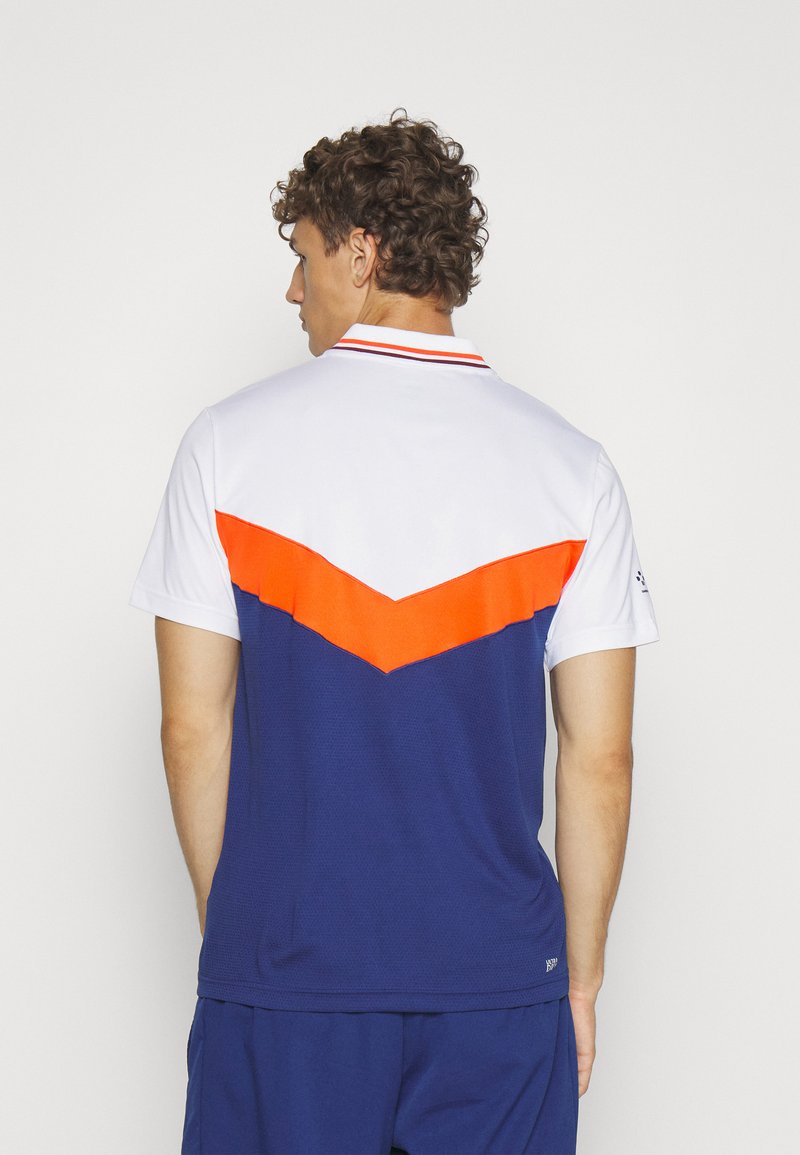 Polo à manches courtes avec un haut blanc, un corps bleu et un motif en chevrons orange. Conçu en tissu texturé avec un col.