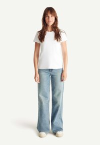 Camiseta de algodón blanca con un corte relajado, combinada con jeans de talle alto de campana en un azul claro. El calzado presenta un diseño sencillo en crema.