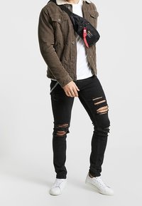 Brun kordflorsjacka med teddykrage, vit t-shirt, rivna svarta jeans, svart axelremsväska och vita sneakers.