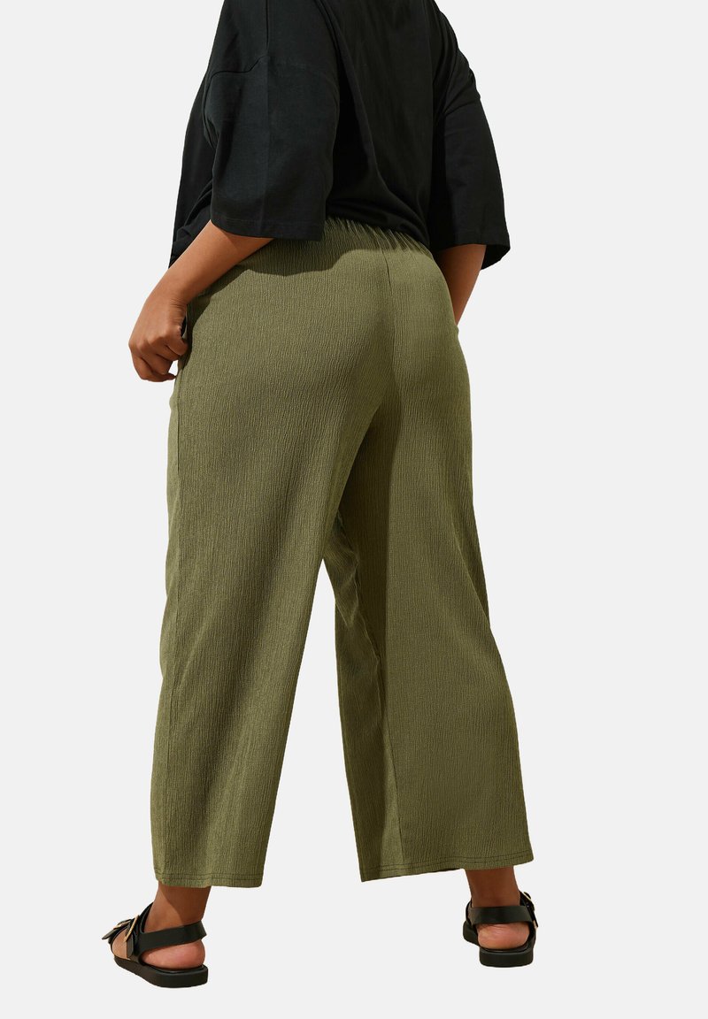 Pantalons larges vert olive, tissu texturé, taille élastique, longueur cropped, poches latérales, associés à des sandales noires.