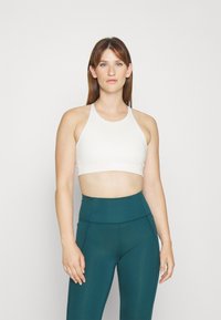 Világos színű, pántos crop top, amely magas derekú, tenger zöld leggingszel van párosítva. Mindkettő rugalmas, sima anyagból készült.