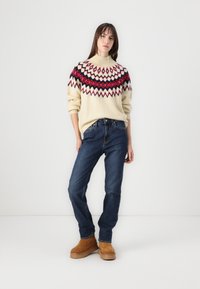 Knit sweater in cream with multicolored geometric pattern; blue jeans; tan boots with platform; relaxed fit, long sleeves, ribbed collar.