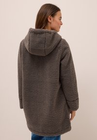 Manteau en polaire gris avec capuche, présentant une surface texturée et une coupe légèrement oversize. Manches longues et ourlet arrondi.