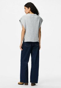 Ljust grå stickad tröja med korta, vida ärmar, ihop med mörkblå vida jeans och bruna klackstövlar. Strukturerad tyg, sidoflikar.