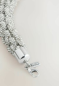 Silbernes geflochtenes Armband mit funkelnden Texturen, metallischem Verschluss und zusätzlichen Beschlägen. Glatte Oberfläche mit reflektierender Qualität.