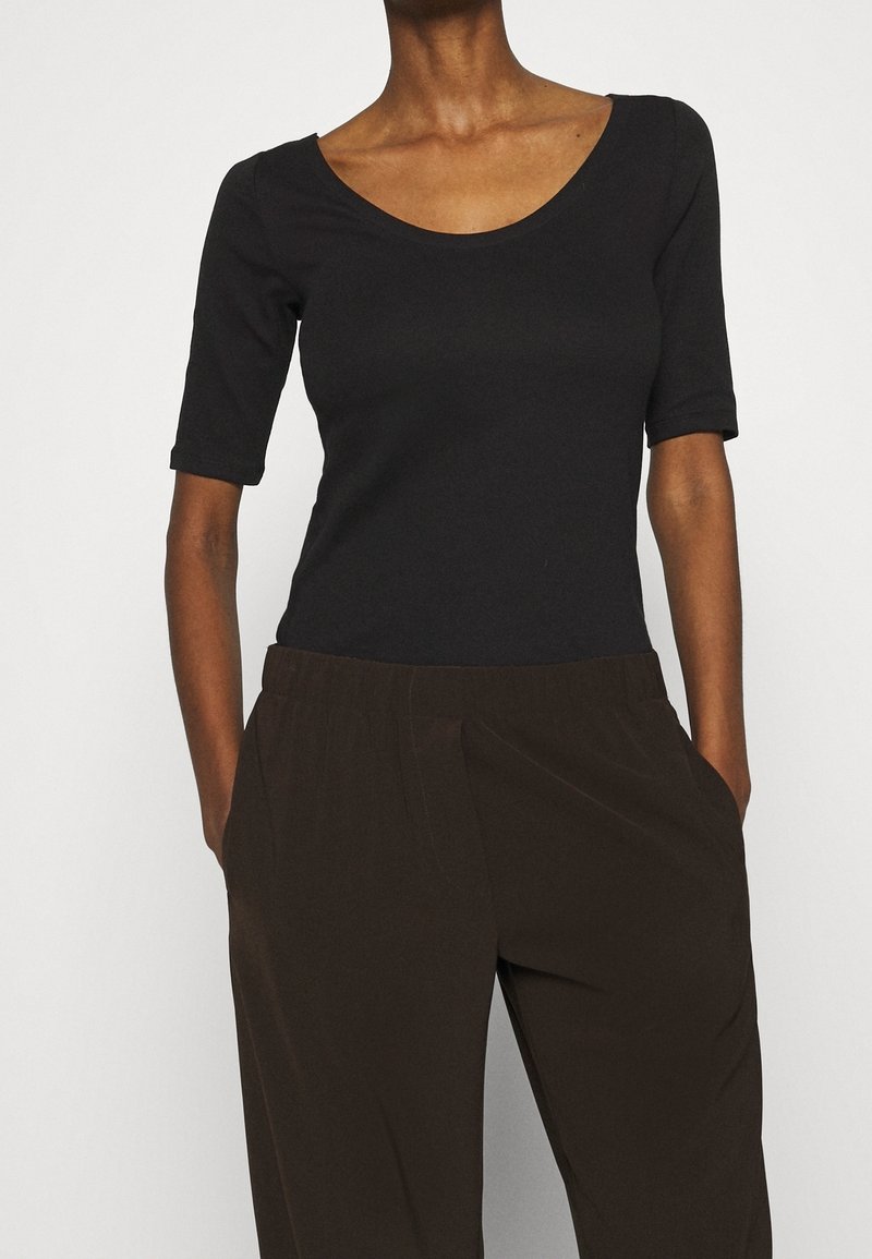 Haut noir à manches courtes avec un col en U, confectionné dans un tissu lisse et extensible. Associé à un pantalon large marron avec des poches latérales.