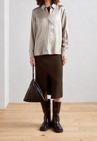 Satin-silberne Bluse, gerippter olivfarbener Rock, schwarze kniehohe Stiefel und eine dreieckige schwarze Ledertasche mit Reißverschlussdetails.