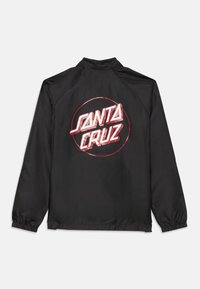 Svart vindjacka med en stor cirkulär grafikhur "SANTA CRUZ" i fet röd text på ryggen. Elastiska mudd och krage.