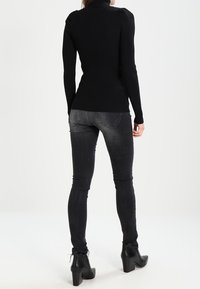 Haut noir côtelé à manches longues avec un col montant ; jean skinny gris clair, porté avec des bottines à talons noires. Texture lisse et coupe ajustée.