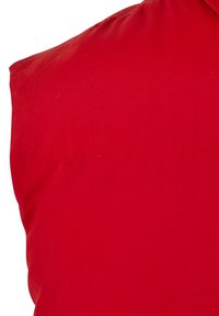 Rotes ärmelloses Kleidungsstück mit glattem Stofftextur, das eine Nahtdetail entlang der Schulter aufweist.