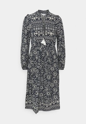 Navy ja valge mustriga kleit pikaotse, kõrge kaelusega ja kogutud vöökohaga. Omab tussli detaile ja keerulisi geomeetrilisi kujundusi.