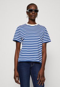 Stribet kortærmet t-shirt i blå og hvid, lavet af bomuldsmateriale, runde udskæring, afslappet pasform, parret med mørke jeans og rektangulære solbriller.