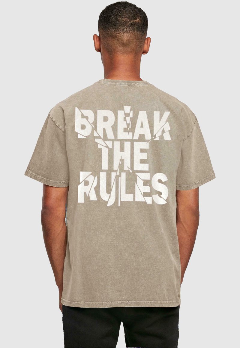 Kortærmet beige T-shirt med løs pasform, der har fed hvid tekst på bagsiden: "BRYDE REGLERNE," med en slidt effekt.