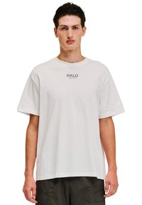 Hvid kortærmet t-shirt lavet af bomuld, med et trykt logo "HALO" på brystet. Simpelt, afslappet design med en løs pasform.