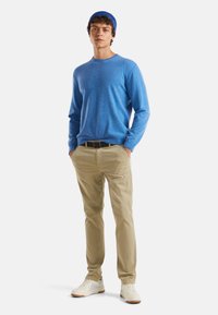 Niebieski sweter z dzianiny z okrągłym dekoltem, beżowe chinosy i białe trampki. Postać nosi niebieską czapkę beanie; luźny krój.