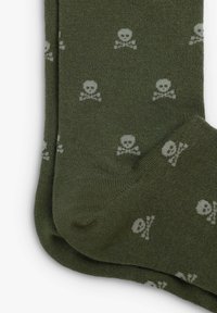 Vihreät puuvillakot, joissa on toistuva kuvio valkoisista pääkalloista ja ristiluista, sileä pinta ja ribbauskorostuksia.