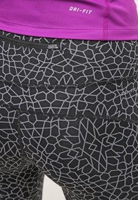 Leggings negros Dri-FIT con un patrón geométrico gris, que cuentan con un bolsillo con cremallera y costuras planas para mayor comodidad. La cinturilla es alta y elástica.