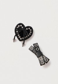 Zwart accessoire in de vorm van een hart met metalen oogjes en een trekkoord. Extra zwart strikvormig stuk met ronde accenten.