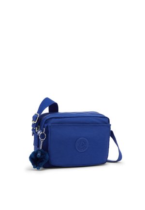Pequeño bolso azul bandolera con correa ajustable, bolsillo delantero, cremallera y un llavero de mono de peluche unido al tirador de la cremallera.