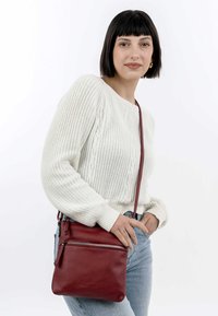 Rote Leder-Crossbody-Tasche mit einer Reißverschlusstasche auf der Vorderseite. Sie hat eine glatte Textur und einen verstellbaren Riemen.