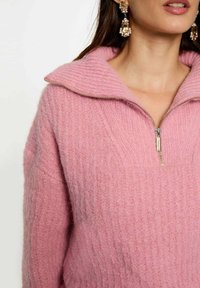 Maglione zip-up rosa con texture a coste, colletto oversize e dettaglio della cerniera in argento. Il materiale morbido aumenta il calore e il comfort.