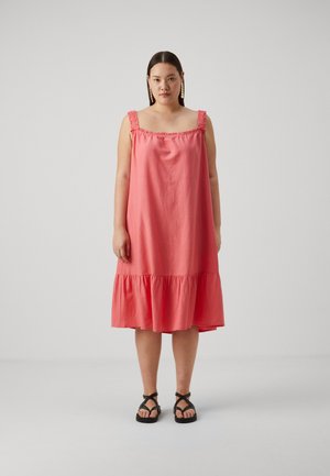 Coral-colored sleeveless dress with ruffled straps, a square neckline, and a flared tiered skirt. Worn with black strappy sandals.