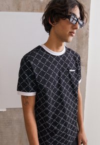 Black short-sleeve t-shirt with white geometric pattern and trim. Features small logo patch on chest; made of smooth fabric. Casual fit.