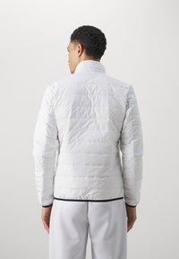 Hvid puffy jakke med høj krave, horisontalt quiltet design og en sort-accentueret kant. Glat tekstur med et let udseende.