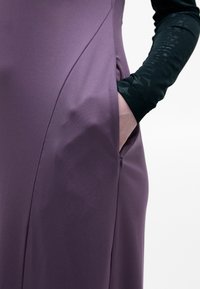 Violeta kleita ar gludu, elastīgu audumu. Iekļauts sānu kabata un sarežģīta melna teksturēta piedurkne. Vienkāršs, piegulošs dizains.