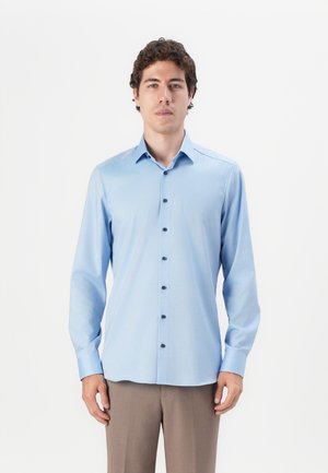 Light blue button-up shirt with a subtle textured pattern, long sleeves, and dark buttons. Worn with beige trousers.