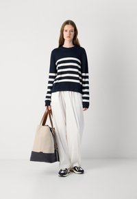 Sweater às riscas azul-marinho e brancas, de corte relaxado, combinado com calças brancas. Bolsa bege com pega castanha, de base escura e sapatos desportivos.