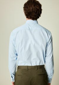 Cămașă albastru deschis cu guler și mâneci lungi, textură netedă și un model subtil, asortată cu pantaloni verzi măslinii care au buzunare la spate.