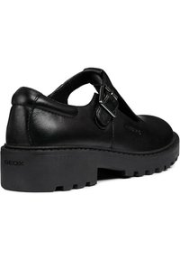 Zapato de piel negra con correa de hebilla en la parte trasera, puntera redondeada, diseño recortado y suela gruesa con dibujo. Logotipo grabado en el lateral.