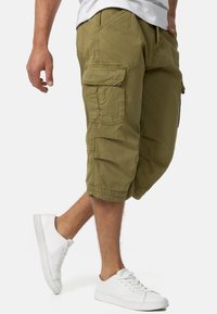 Shorts cargo vert olive en coton, dotés de plusieurs poches, de détails cousus et d'une coupe décontractée, associés à des baskets blanches.