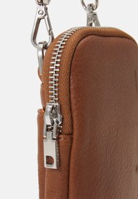 Brązowa skórzana torba z srebrnym zamkiem błyskawicznym i metalowym zapięciem przymocowanym do paska na białym tle.