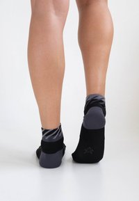 Schwarze und graue Knöchelsocken mit einem Muster am Saum. Die Socken weisen kontrastierende Texturen auf und haben ein Logodesign auf der Rückseite.
